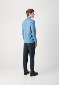 Helles blaues Langarmpolo, dunkelblaue schmal geschnittene Hose und schwarze Schuhe. Glatte Textur, minimalistisches Design und taillierte Silhouette.