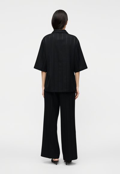 Pantaloni neri a gamba larga abbinati a una camicia oversize con colletto coordinata. Presentano righe verticali sottili, tessuto morbido e vestibilità comoda.