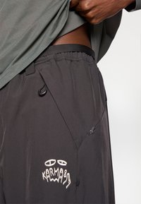 Zwarte shorts met een gestructureerde stof, voorzien van een elastische tailleband en een wit geborduurd logo. Voorzien van een trekkoord en pocketdetails.