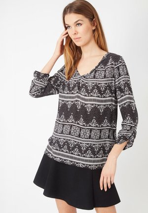 Blusa negra con estampado, con escote en V, mangas tres cuartos y detalle fruncido, combinada con una falda negra acampanada.