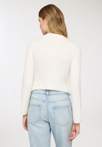 Maglione bianco corto in tessuto morbido, con maniche lunghe e scollo rotondo, abbinato a jeans a vita alta di colore azzurro chiaro.