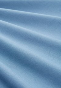 Jasnoniebieska tkanina o gładkiej teksturze, z delikatnymi fałdami. Materiał wydaje się miękki i lekki, o jednolitym kolorze.