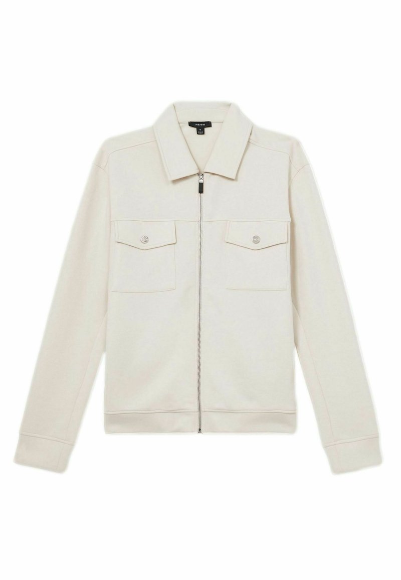 Lyse beige zip-jakke med krave, to brystlommer og ribbede manchetter. Fremstillet af blødt stof med en glat tekstur og diskret syning.