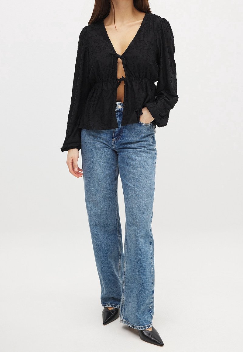 Haut noir à motifs floraux avec un décolleté en V profond et une fermeture à nouer à la taille. Associé à un jean évasé bleu clair et des chaussures noires à bout pointu.