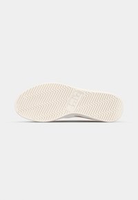 Sole of a sneaker with a zigzag tread pattern. Color is cream with a smooth texture. Brand logo visible on the heel area.
