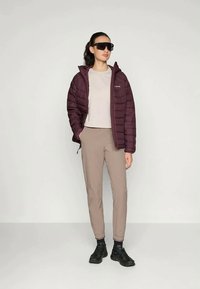 Bordowa kurtka ocieplana, jasnoszara bluzka, beżowe spodnie i czarne buty. Obecne okulary przeciwsłoneczne. Prosty design i dopasowany krój.