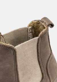 Botă din suede maroniu, cu o textură netedă și panouri laterale elastice. Interiorul este captușit cu un material moale și pufoș. Dispune de o bandă de mers pe spate.