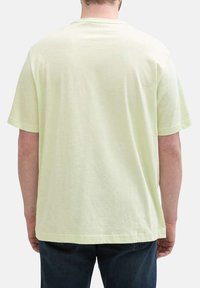 T-shirt vert clair à manches courtes en tissu doux, avec une coupe décontractée et un col rond simple. Pas de logos ni de motifs visibles.