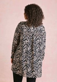 Langsleeve shirt in zwart en crème met een zigzagpatroon. Lichtgewicht stof, relaxed fit, zijsplitten en een detail van de achternaad.