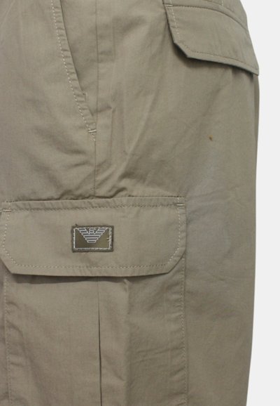 Pantaloni cargo beige con vestibilità normale, caratterizzati da più tasche, dettagli cuciti e un logo sul lato sinistro vicino alla cintura.