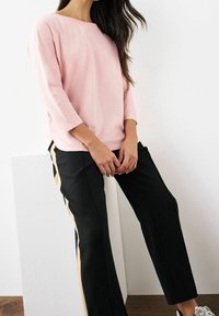 Top de manga larga rosa claro con un escote amplio, combinado con pantalones negros que tienen rayas laterales beige, mostrando un ajuste relajado y una textura suave.