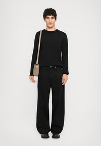 Must be a black long-sleeve shirt, milleka ka ümara kaelusega, koos laia mustade pükstega. Mudel hoiab käes väikest pruuni rihmaõlapaela kotti.