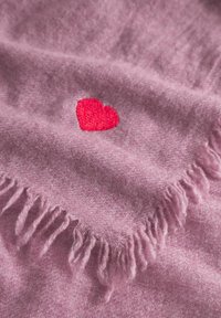 Écharpe rose clair avec un motif de cœur rouge. Fabriquée dans un matériau doux avec des bords à franges, mettant en valeur une texture fine.