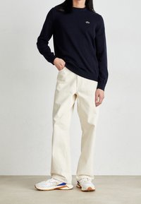 Marinblå tröja med ribbade muddar, krämfärgade vida byxor och vita sneakers med marinblå och orange detaljer. Minimalistisk design; rena linjer.