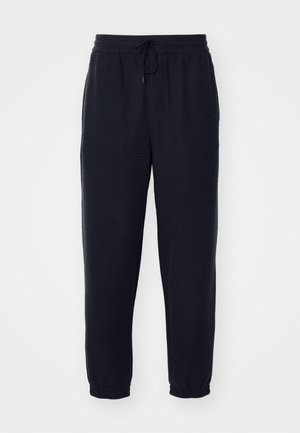 Pantalons de jogging noirs en tissu texturé, dotés d'une taille élastique avec un cordon de serrage et des chevilles fuselées.