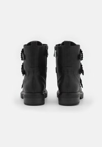 Stivaletti neri in pelle con una texture liscia; adornati con dettagli decorativi sui lati e una suola in gomma robusta. Vista posteriore.