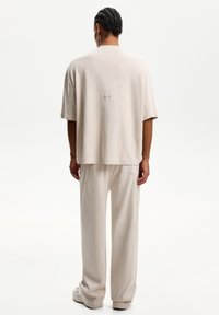 Beige cotton t-shirt with a relaxed fit. Features short sleeves and a small logo print on the upper back. Paired with matching trousers.