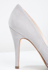 Escarpin à talons hauts en daim gris avec un bout pointu, un talon aiguille mince, un intérieur en cuir lisse et une semelle beige.