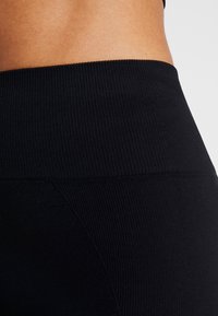 Czarne, prążkowane legginsy o wysokim stanie z gładką teksturą i szerokim pasem, z bocznym panelem dla dodatkowego detalu.
