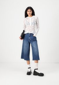 Hvit blonde langermet topp med blomstermønster, parret med løse blå denim culotte-shorts. Svart plattform sko og hvite anklestrømper.