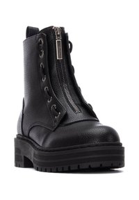 Botín negro de cuero con acabado texturizado, cremallera lateral y detalles de cordones. Suela gruesa con un patrón de banda de rodadura resistente.