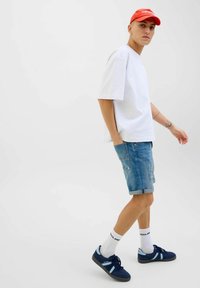 Witte oversized t-shirt, lichtblauwe denim shorts met opgerolde mouwen, blauwe sneakers met lichte accenten, en witte sokken met zwarte letters.
