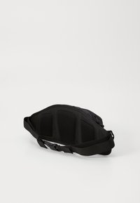 Black waist bag with adjustable strap and mesh padding on the back side, resting on a white surface.