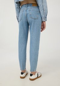 Jeans in denim blu chiaro con vita alta, gamba affusolata e due tasche posteriori. Abbinati a sneakers bianche con dettagli neri.