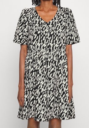 Woman wearing a black and white patterned short-sleeve dress with a V-neck and buttons down the front.