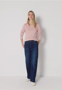 Lichtroze top met lange mouwen en ronde hals, gecombineerd met donkere blauwe wijdlopende jeans. Het model draagt witte sneakers. Eenvoudige, casual outfit.