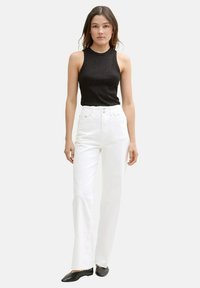 Top negro sin mangas con un brillo sutil, combinado con jeans blancos de pierna recta de cintura alta y zapatos planos negros. Diseño simple y limpio.