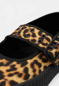 Leopárdmintás slip-on cipő fekete pánttal és szegecsekkel, gumiból készült, kerek orral és texturált fekete talppal.