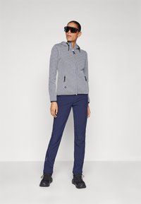 Giacca con zip e cappuccio, a fantasia, in bianco e nero, abbinata a pantaloni blu navy e calzature nere. Presenta tasche laterali e un design aderente.