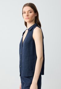 Marineblauw mouwloos linnen shirt met een V-hals, knopen aan de voorkant en een kraag. Soepele textuur met een relaxte pasvorm.