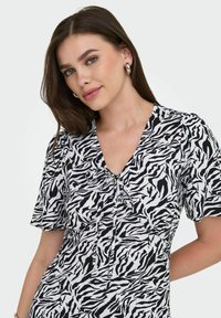 Robe à imprimé zèbre noir et blanc avec des manches courtes, décolleté en V et un détail à nouer à l'avant. Tissu léger avec une texture lisse.