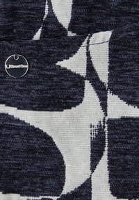 Tissu bleu foncé et blanc avec de grandes formes abstraites et une petite étiquette métallique ronde portant l'inscription "Street One" attachée.