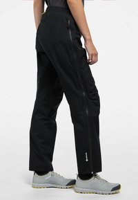 Svarta vandringsbyxor har en dragkedja på sidan och en slät yta. De är ihopparade med grå skor och en åtsittande topp.