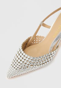 ασημένιο παπούτσι slingback με μυτερή μύτη, σχέδιο με ανοίγματα και καλυμμένο με στρογγυλά αντανακλαστικά στρας.