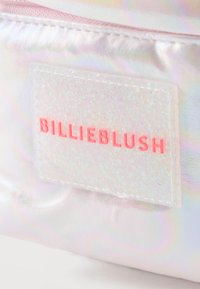 Κοντινό πλάνο ετικέτας υφάσματος με ολογραφικό φόντο και ανάγλυφο ροζ κείμενο "BILLIEBLUSH" σε μια λαμπερή, ιριδίζουσα ορθογώνια επιφά νεια.