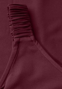 Tessuto bordeaux con texture arricciata su un lato, superficie liscia sull'altro, e un dettaglio di cucitura lungo il bordo.