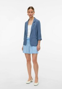 Mėlynas švarkas su susuktais rankovėmis, baltas topas be rankovių ir mėlynai dryžuotos šortai. Balti slingback aukštakulniai bateliai užbaigia aprangą.