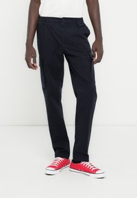 Μαύροι cargo παντελόνες με πλαϊνές τσέπες, ελαστική μέση και φερμουάρ. Συνδυασμένο με κόκκινα καμβά παπούτσια, με λευκές σόλες και κορδόνια.