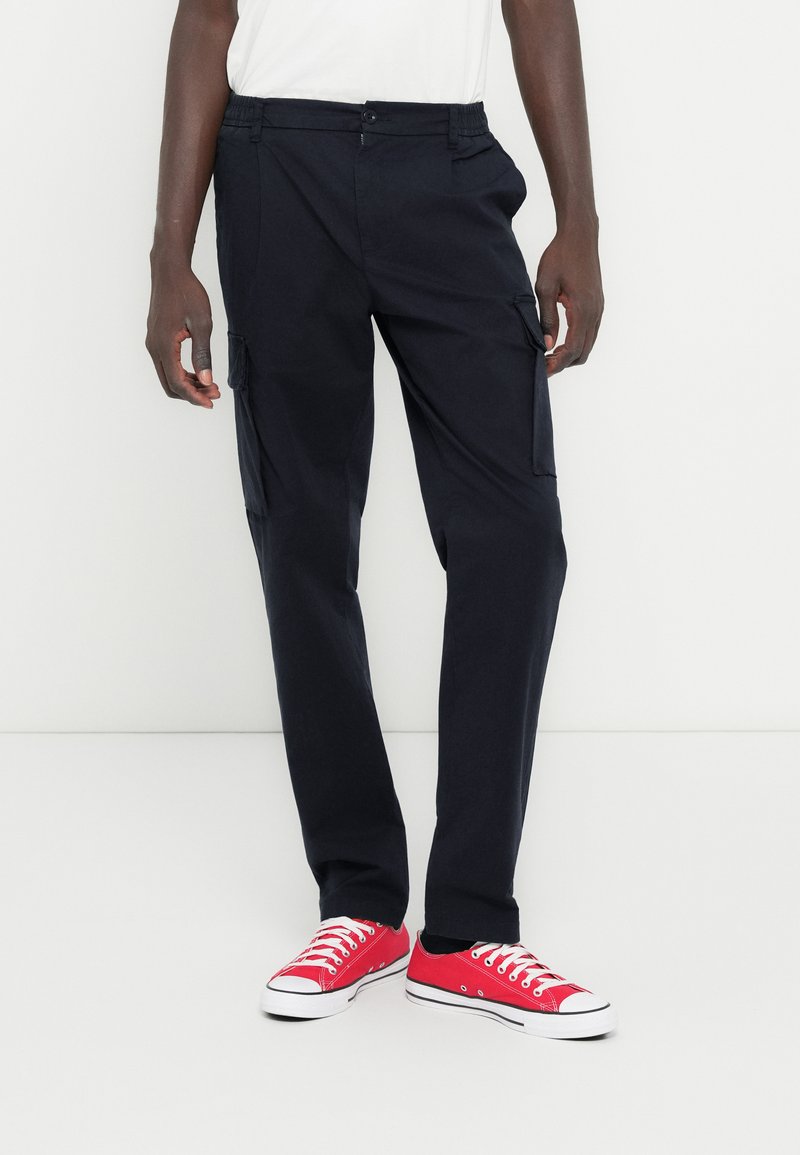 Μαύροι cargo παντελόνες με πλαϊνές τσέπες, ελαστική μέση και φερμουάρ. Συνδυασμένο με κόκκινα καμβά παπούτσια, με λευκές σόλες και κορδόνια.