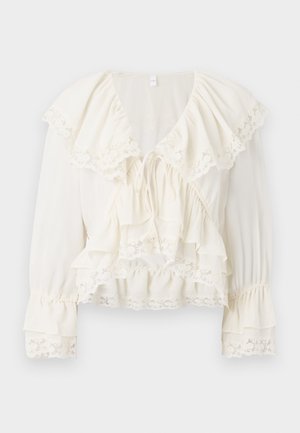 Hvit bluse med lagdelt, volang-design, blondekant på ermene og kanten, samt V-hals med snøring.