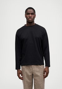 Crna dugoslabna majica od mekog materijala s okruglim izrezom, uparen s laganim smeškim hlačama teksturiranog izgleda. Jednostavan, opušten kroj.