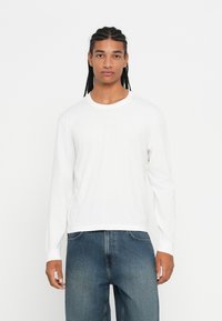 Wit T-shirt met lange mouwen, gemaakt van katoen, met een ronde halslijn en een ontspannen pasvorm, gecombineerd met blauwe denim jeans in een losse stijl.