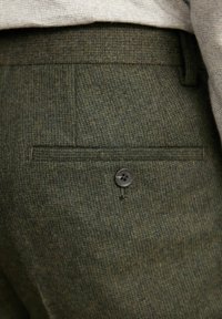 Grüne, strukturierte Hose mit einer Gesäßtasche, die mit einem einzelnen dunklen Knopf versehen ist, und einem dezenten gemusterten Stoff. Taillierter Schnitt für zusätzlichen Komfort.