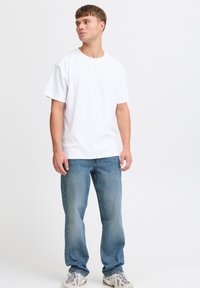 Camiseta de algodón blanca de manga corta, combinada con jeans de color azul claro. El conjunto se completa con zapatillas grises y blancas.
