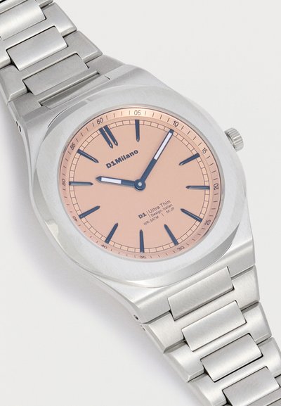 Ασημένιο μεταλλικό ρολόι χειρός με ροζ καντράν, σκούρους δείκτες ώρας και δύο λευκές αιχμές στο δείκτη που δείχνουν 9:06, ορατό μεταλλικό λουρί με κρίκους.