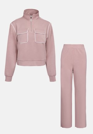 Helles rosa passendes Trainingsoutfit bestehend aus einem Reißverschluss-Pullover mit zwei Brusttaschen und elastischen Bündchenhosen. Glatte Textur, lässige Passform.